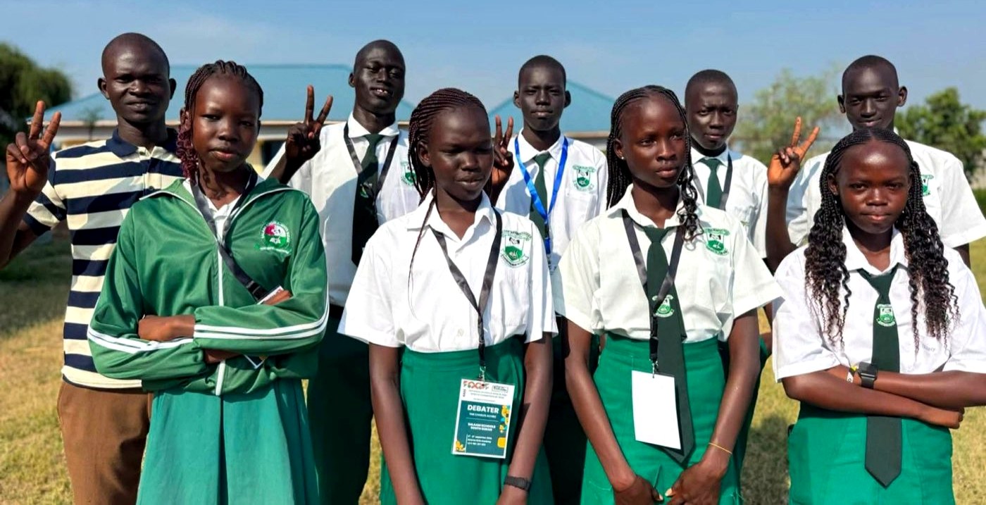 A group of secondary school students in uniform stand together outside their school with a teacher