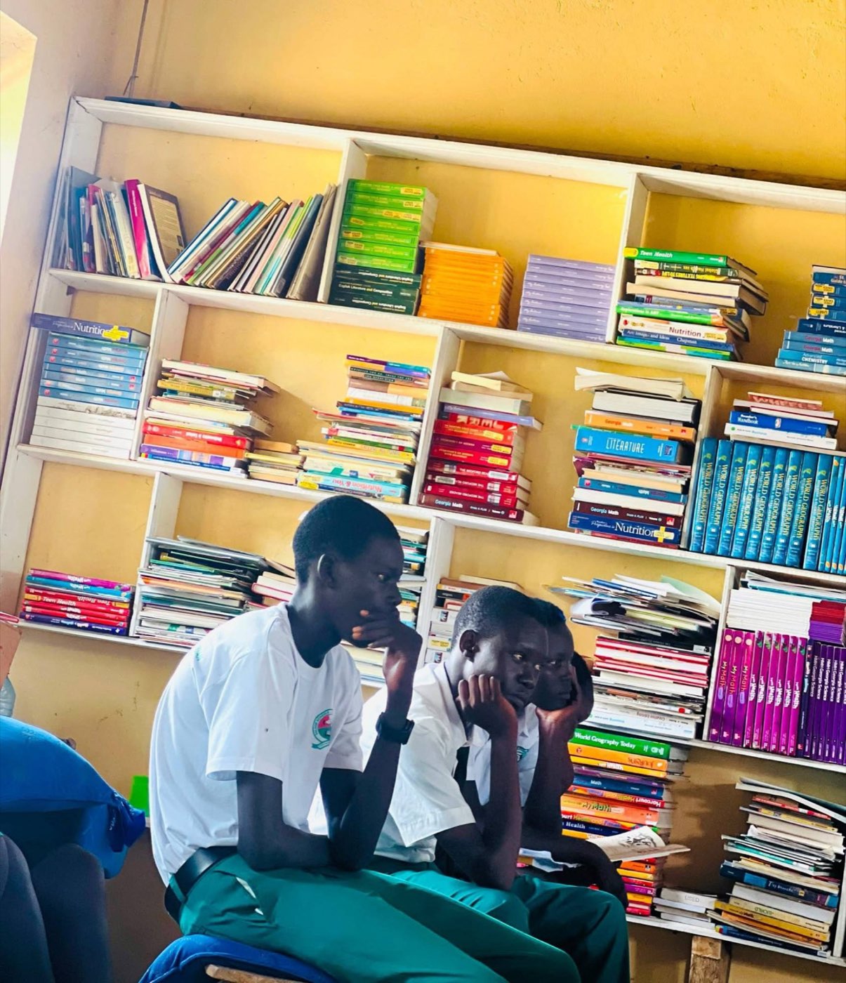 Two students sit thoughtfully in front of a wall of textbooks in a school library