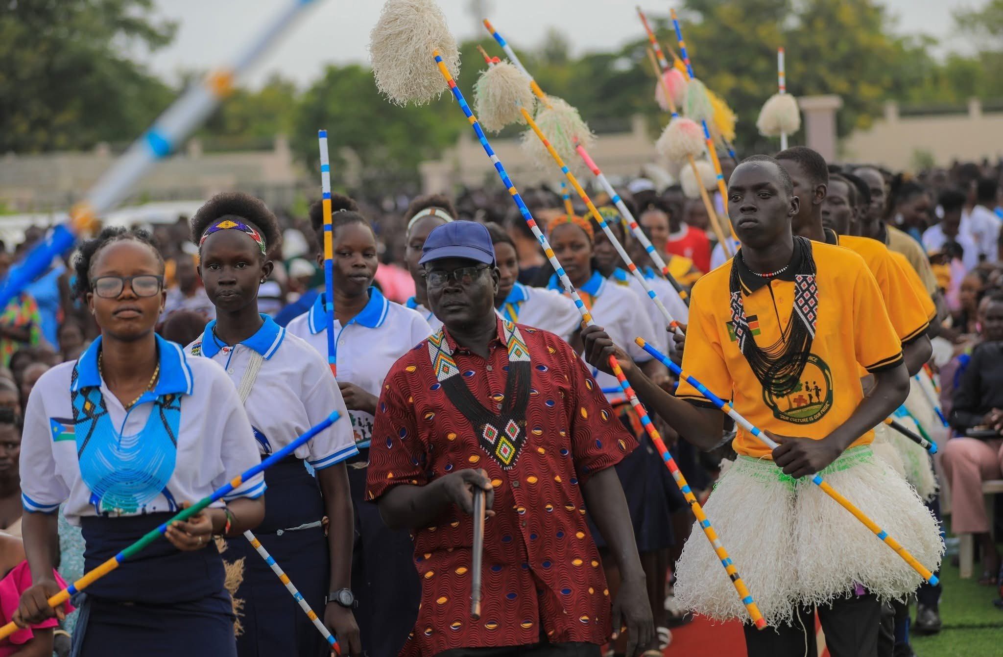 Young people and elders walk together carrying decorated sticks at Peace Cultural Day