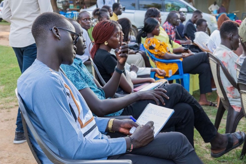 Young South Sudanese participants listen and take notes during an outdoor learning session