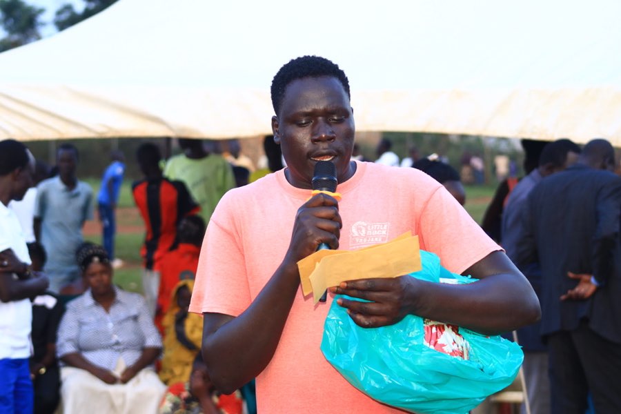 A young South Sudanese man speaks into a microphone in front of a community gathering